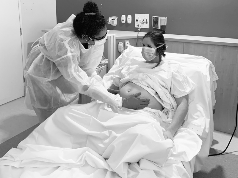 The winning photo, titled Birth: A staff member examining a pregnant woman, both wearing face masks