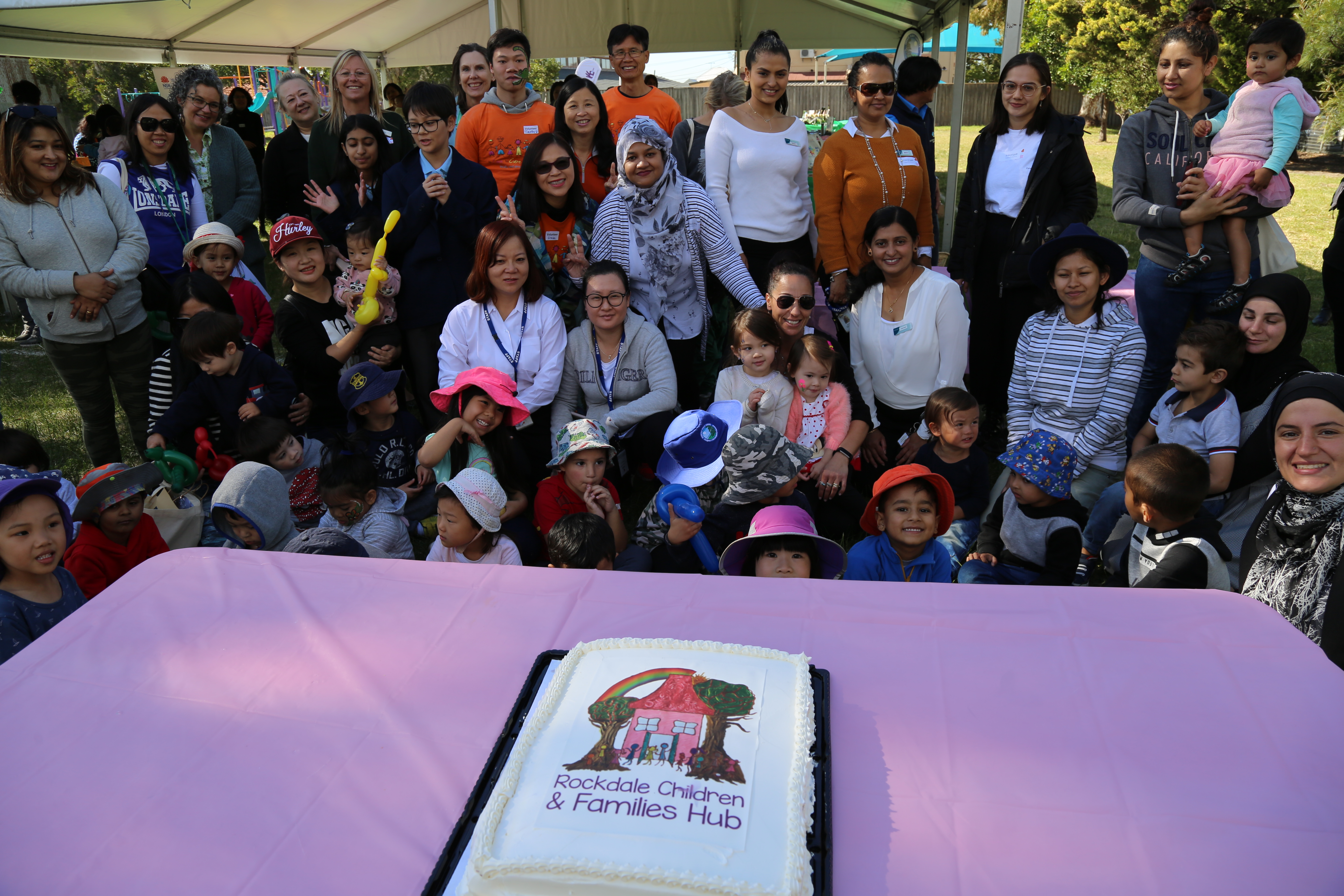 Group photo of families and Rockdale Children and Families Hub service providers with launch cake