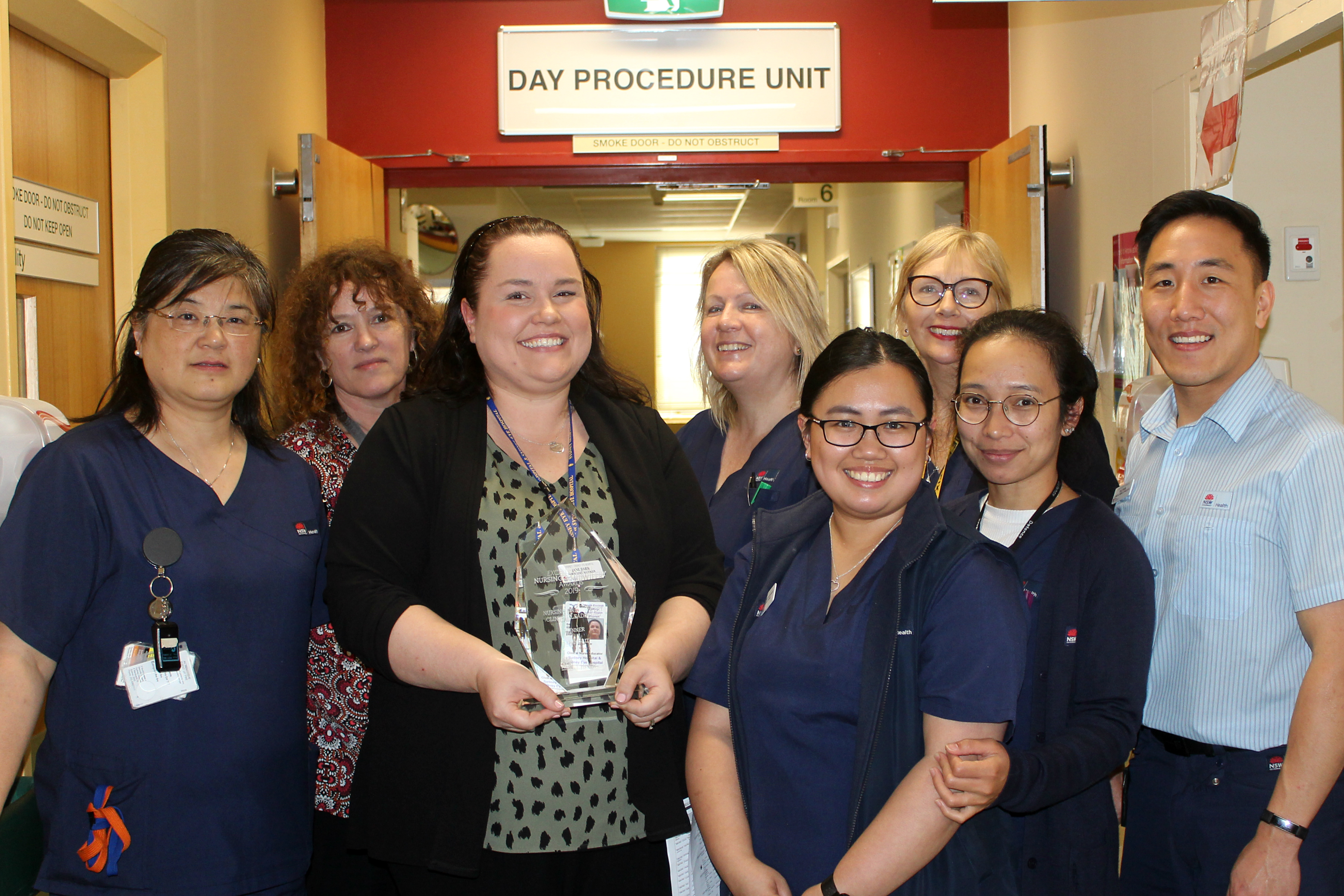 Nurse holding award surrounded by her team in the hall of their ward