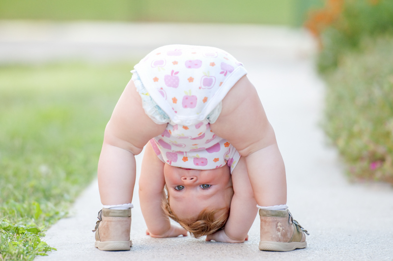 A baby playing upside down on a street 