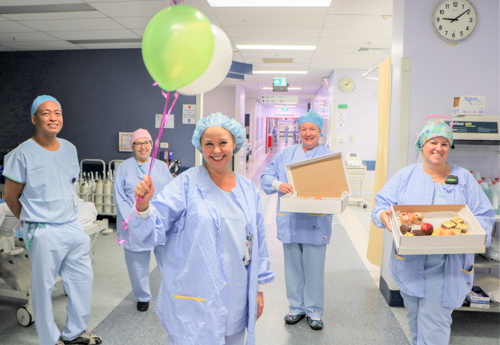 Staff members holding balloons and boxes of morning tea