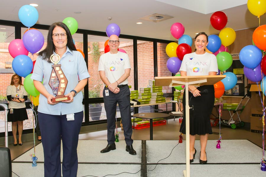 Staff member holding award with two colleagues and balloons in the background 