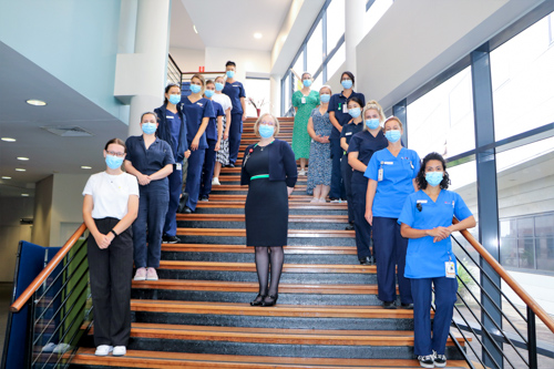 New graduates standing on the lecture theatre stairs with the Director of Nursing and Midwifery Services at The Royal