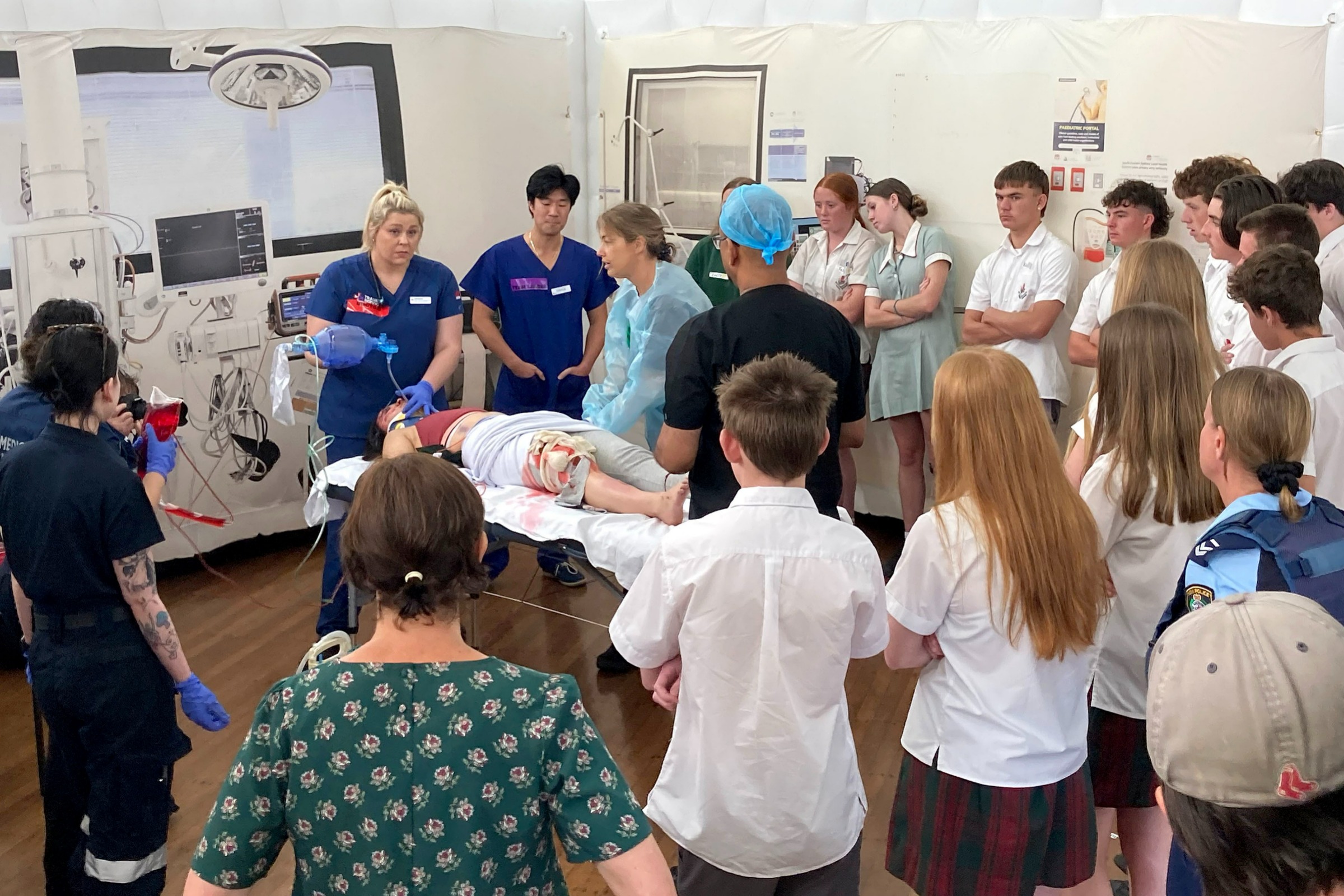 A group of high school students watch a simulated emergency trauma response