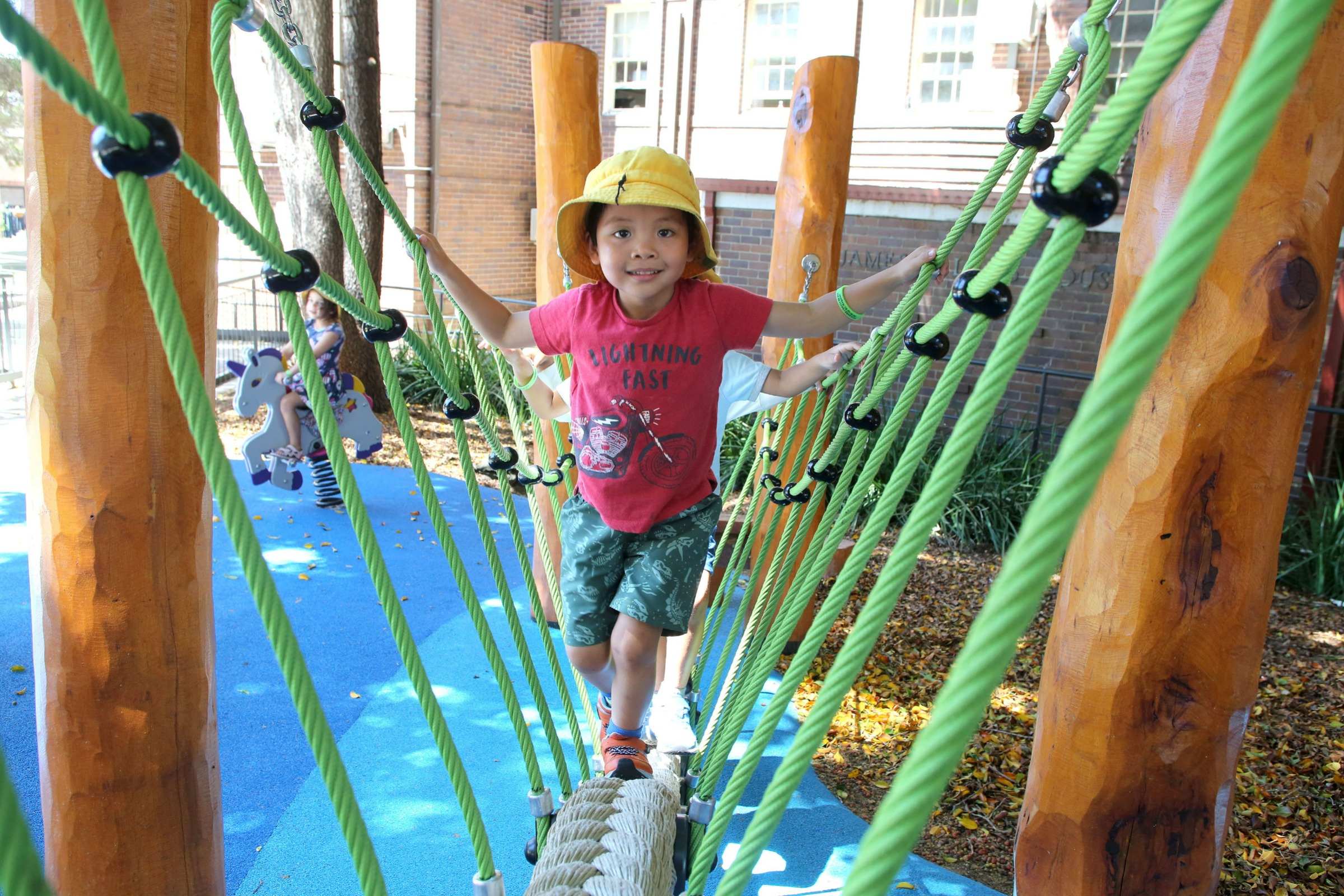 child wearing yellow hat walking across a play equipment bridge