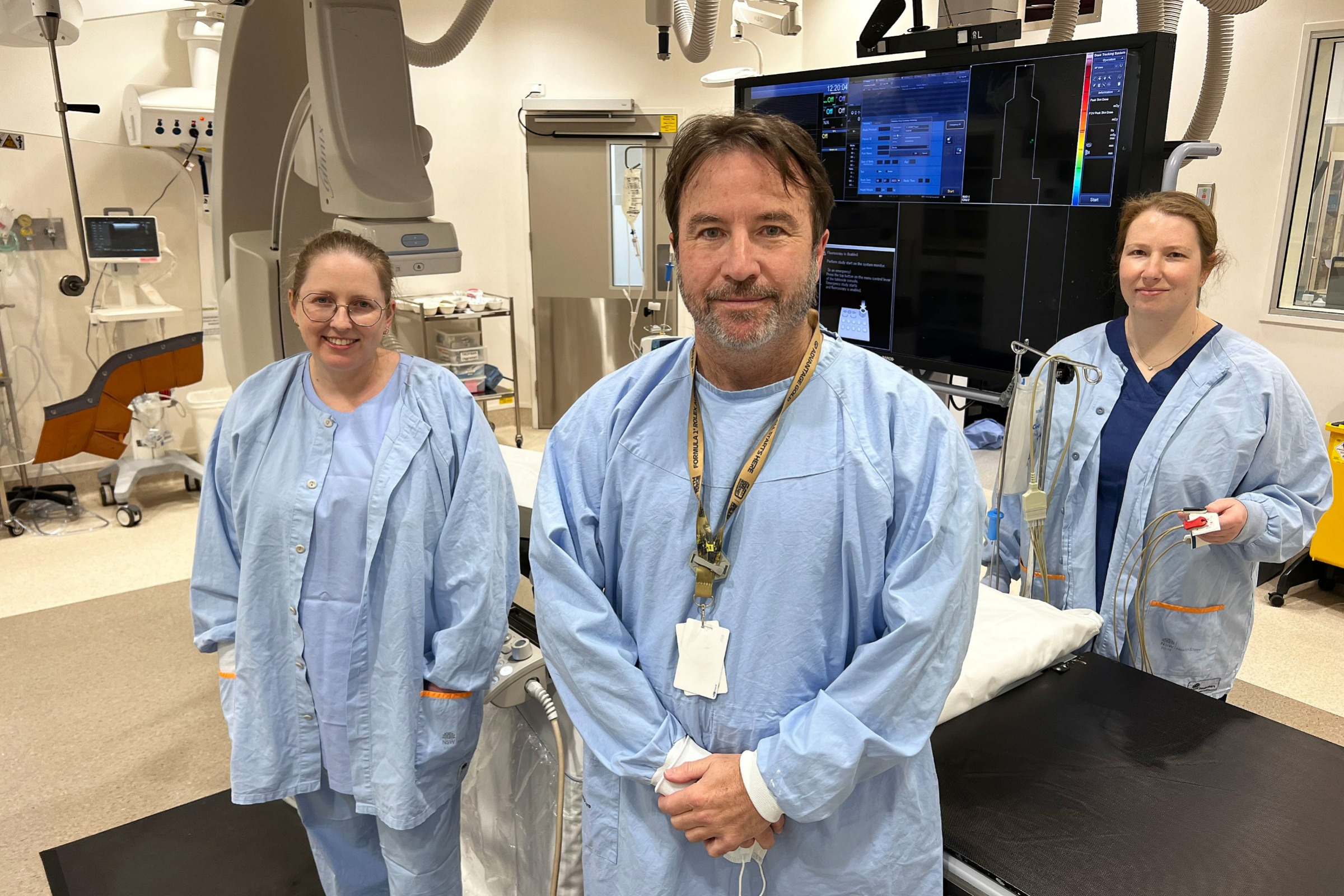 three staff members stand in the cardiac cath lab next to the CT machine