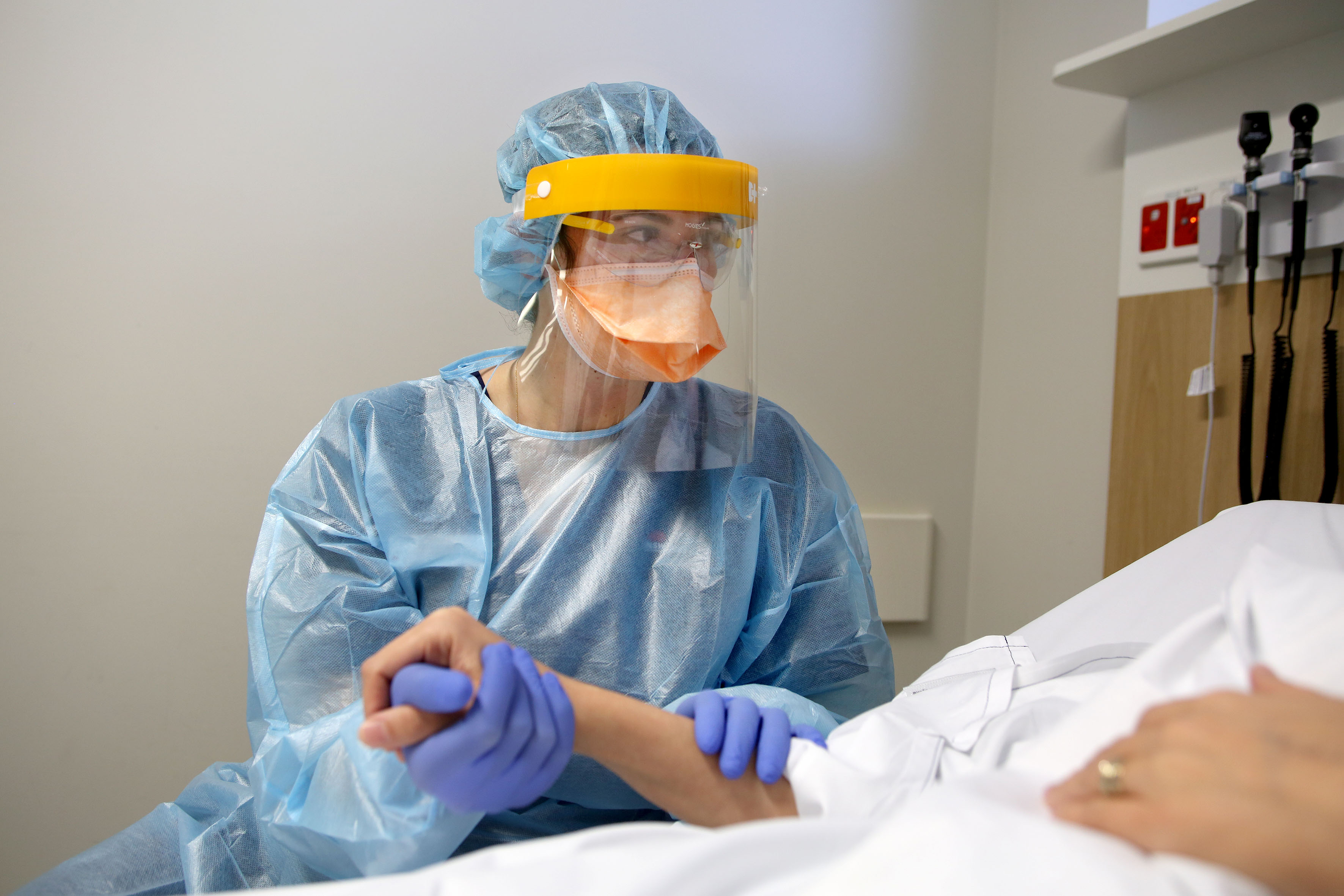 Nurse in PPE holding patients hand