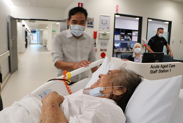 Aged care patient in bed being moved to ward by wards person
