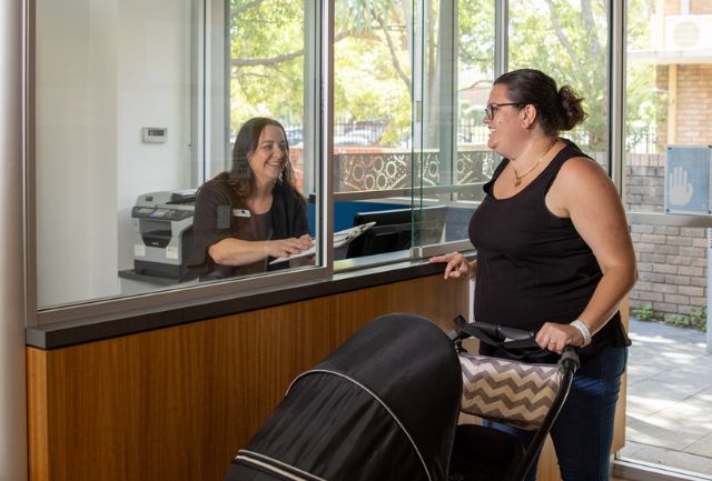 A mother with a pram is greeted by a receptionist