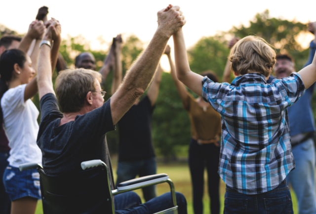 A group of people holding hand including a man in a wheelchair and a child