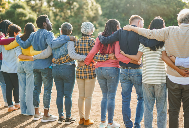 A group of diverse members of the community including in a group hug their backs to the camera