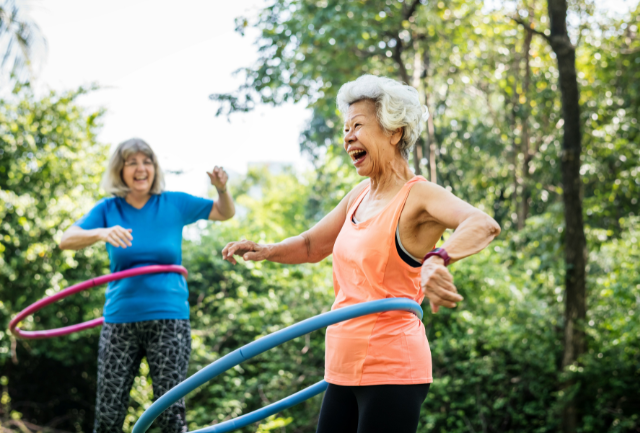 Two older woman laughing and hula hooping in the park