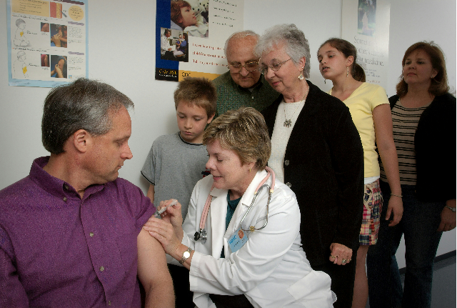 A man was receiving an intramuscular injection in his left shoulder muscle from a trained, registered nurse (RN), while his family was observing from over the nurse's shoulder.