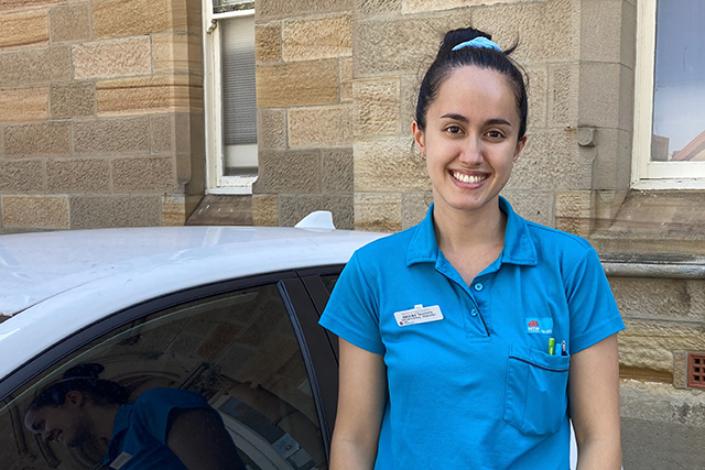 Woman in teal shirt standing next to white car