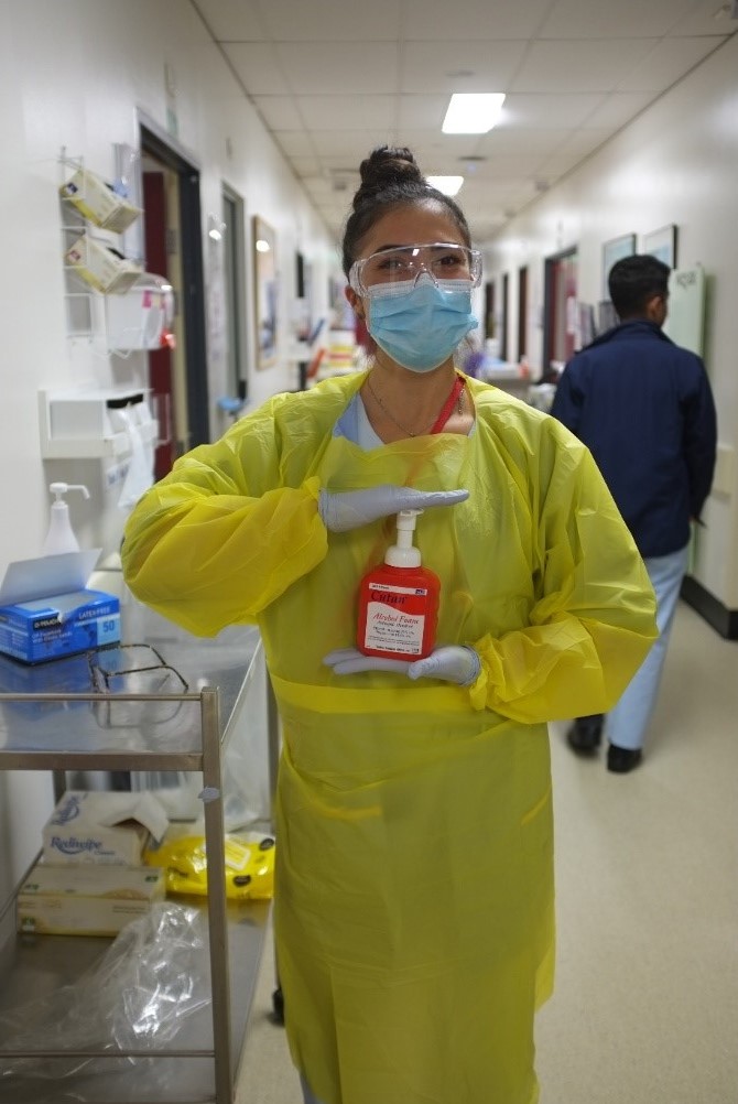 Nurse wearing gown and mask holding alcohol handwash