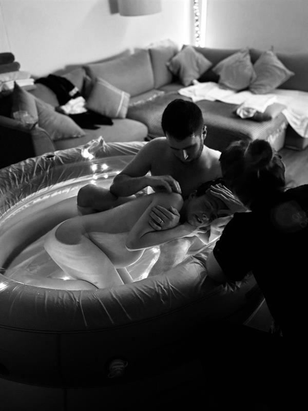 black and white image of woman in the bath during labour being supported by her partner and midwife