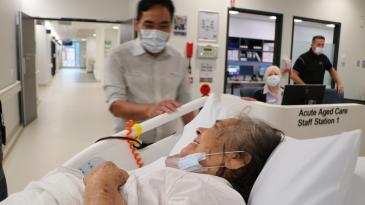 Lady in hospital bed with smiling staff, moving into new building